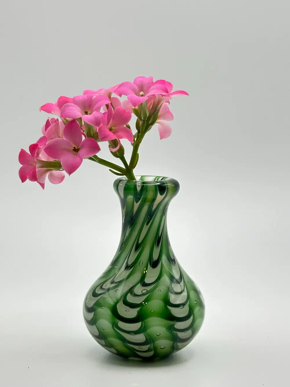 Green patterned glass bud vase holding a stem of bright pink flowers