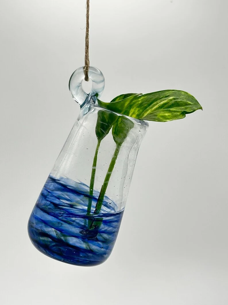 Clear hanging glass vessel with deep blue swirls and a leafy cutting